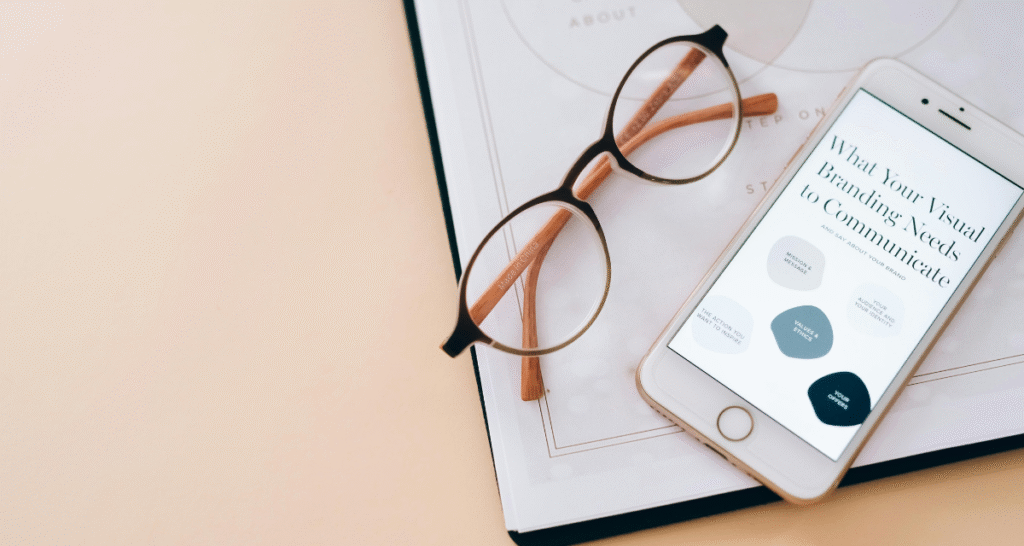 "Eyeglasses resting on a notebook next to a smartphone displaying 'What Your Visual Branding Needs to Communicate,' focused on improving brand recognition and clarity."